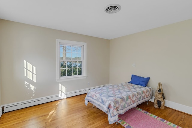 bedroom featuring hardwood / wood-style flooring and a baseboard heating unit