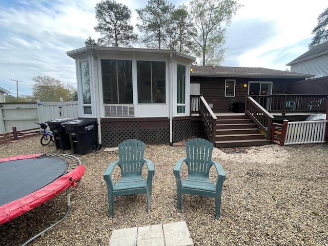 rear view of house with a deck, a trampoline, fence, and a sunroom