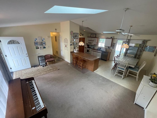 living area featuring vaulted ceiling with skylight, light colored carpet, and ceiling fan
