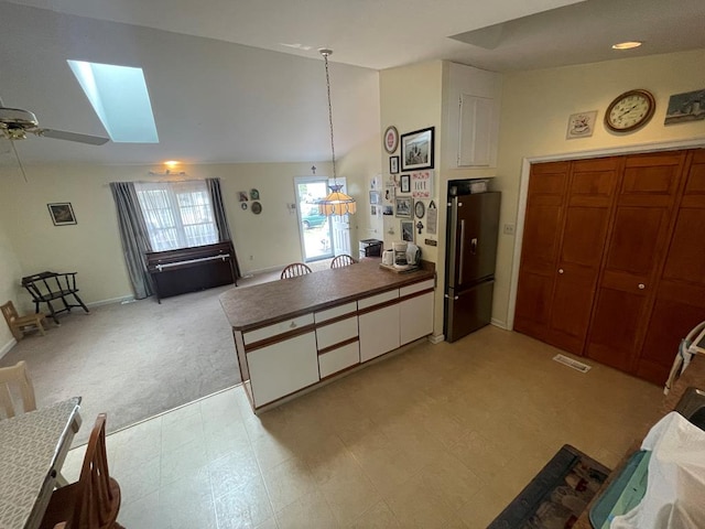 kitchen with vaulted ceiling with skylight, ceiling fan, dark countertops, freestanding refrigerator, and a peninsula