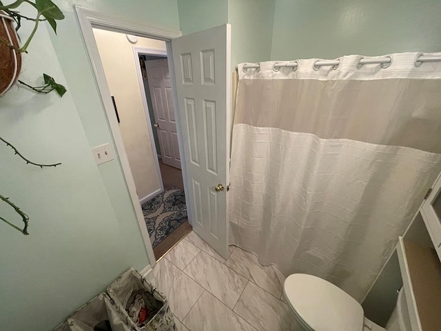full bath featuring toilet, marble finish floor, and a shower with curtain