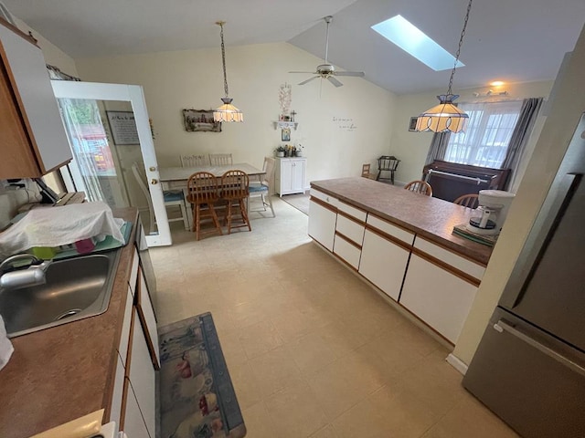 kitchen with a sink, freestanding refrigerator, white cabinetry, and a healthy amount of sunlight