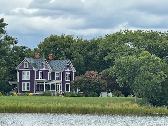 exterior space with a chimney, metal roof, a water view, a standing seam roof, and a front lawn