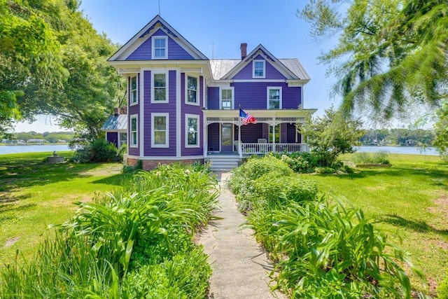 victorian home with a water view, covered porch, a chimney, and a front lawn