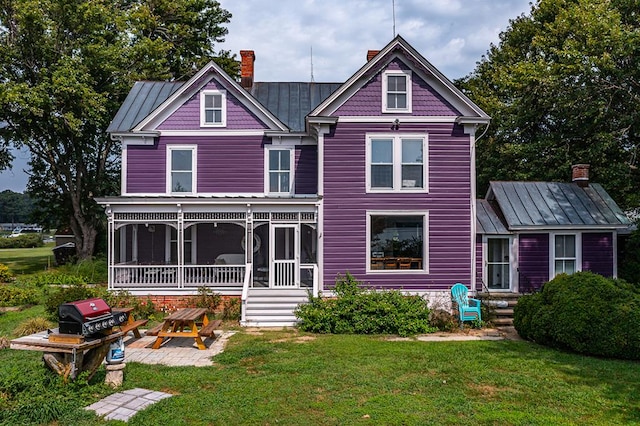 view of front of home with a patio, a sunroom, a chimney, a standing seam roof, and a front yard