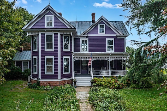 victorian home featuring a standing seam roof, a porch, a chimney, and a front yard