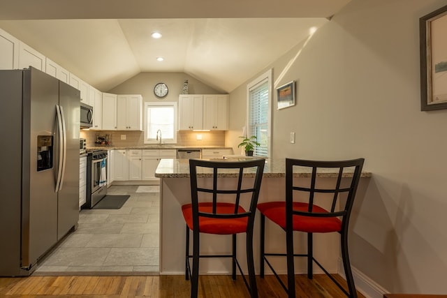 kitchen featuring a kitchen bar, appliances with stainless steel finishes, light stone counters, sink, and white cabinets