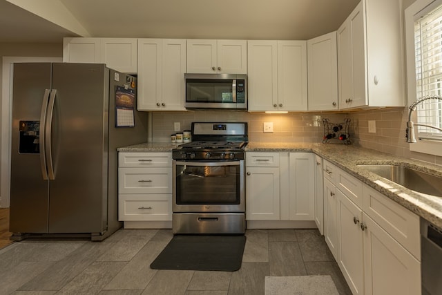 kitchen featuring backsplash, light stone counters, stainless steel appliances, sink, and white cabinetry