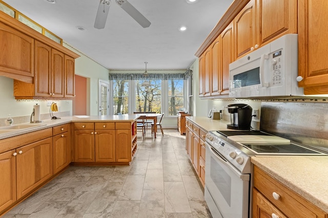 kitchen with kitchen peninsula, ceiling fan with notable chandelier, white appliances, sink, and hanging light fixtures