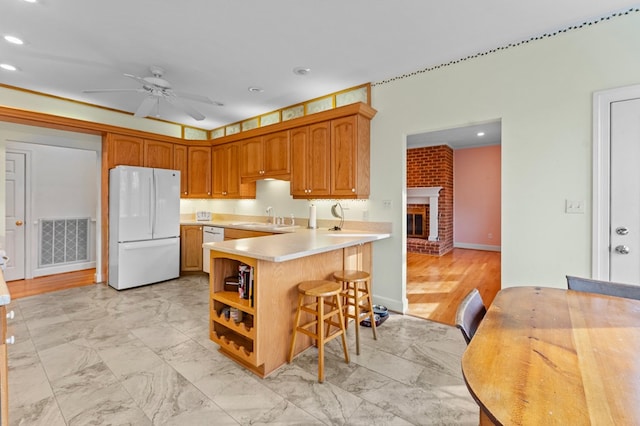 kitchen featuring white appliances, sink, a fireplace, kitchen peninsula, and a breakfast bar area