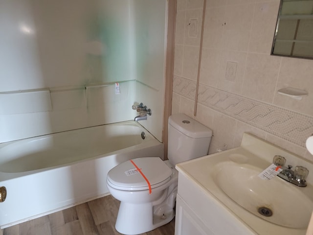 full bath featuring toilet, wood finished floors, tile walls, washtub / shower combination, and vanity
