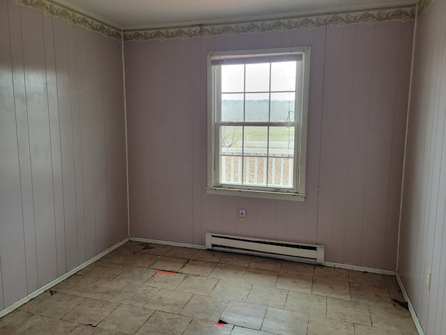 unfurnished room featuring wood walls, a baseboard heating unit, and baseboards