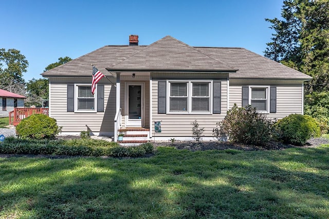 bungalow-style home with a shingled roof, a front yard, and a chimney