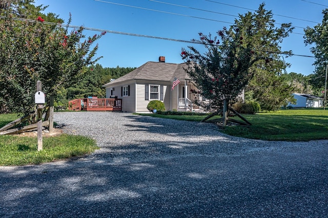 view of front of property featuring a shingled roof, a chimney, gravel driveway, a deck, and a front lawn