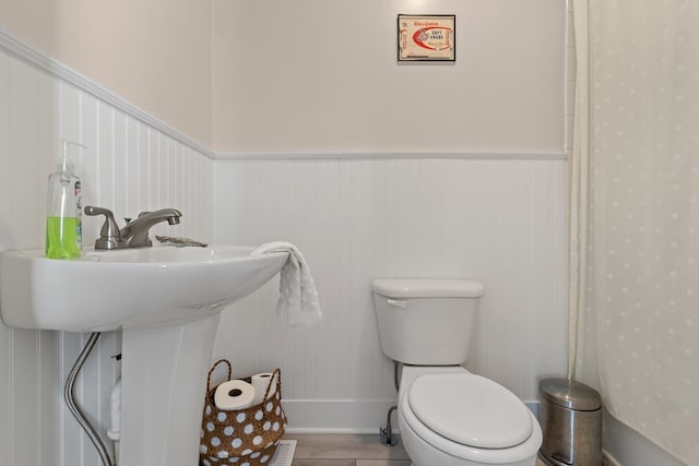 full bath featuring toilet, a wainscoted wall, and a sink