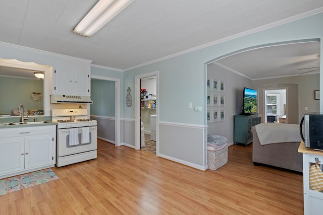 kitchen featuring arched walkways, stainless steel microwave, gas range gas stove, under cabinet range hood, and a sink