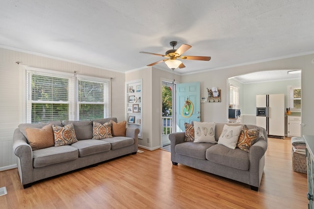 living room with light wood finished floors, arched walkways, baseboards, a ceiling fan, and crown molding