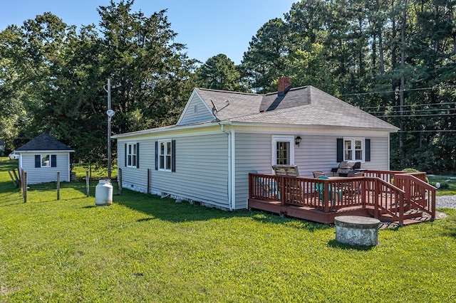 rear view of house featuring a deck, an outbuilding, roof with shingles, a lawn, and a chimney