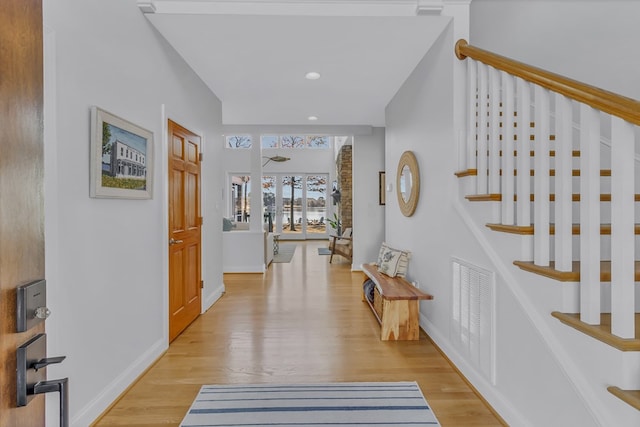 hall featuring light wood-type flooring, visible vents, baseboards, and stairs