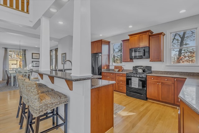 kitchen with dark stone counters, black appliances, plenty of natural light, and light wood-style floors