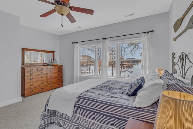 carpeted bedroom with ceiling fan, a water view, visible vents, and baseboards