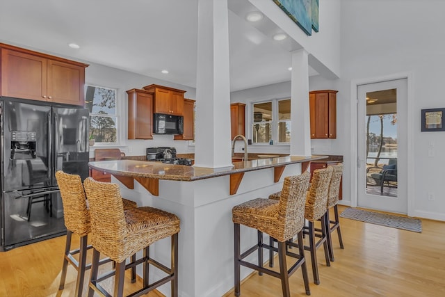 kitchen featuring black appliances, light wood finished floors, dark stone countertops, and a kitchen breakfast bar