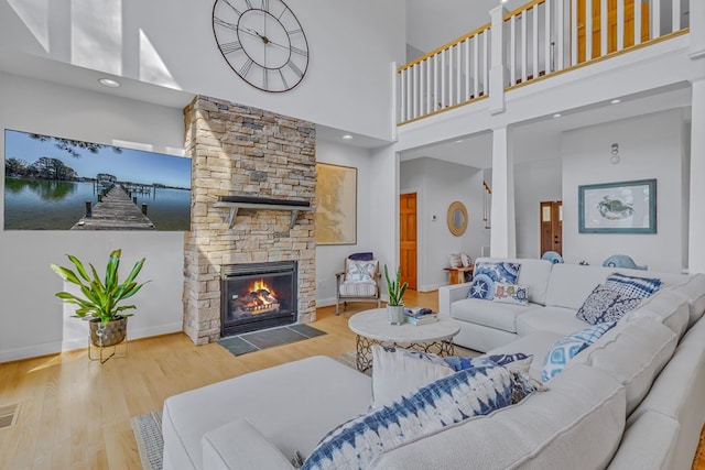 living area with a stone fireplace, wood finished floors, visible vents, a towering ceiling, and baseboards