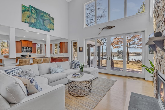 living area featuring a water view, light wood finished floors, a fireplace, and visible vents