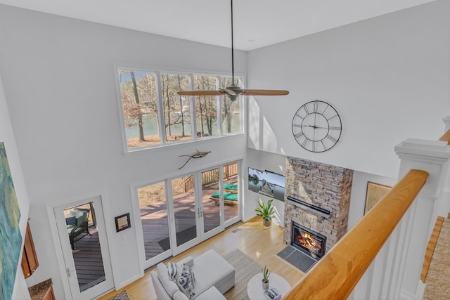 living area with ceiling fan, a stone fireplace, a towering ceiling, and wood finished floors