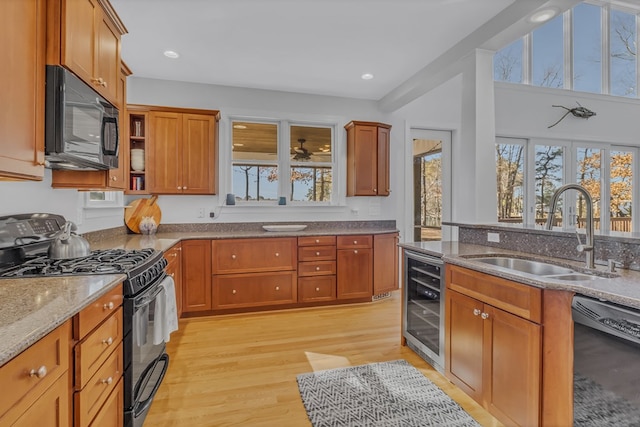 kitchen featuring stone countertops, wine cooler, light wood-type flooring, black appliances, and a sink