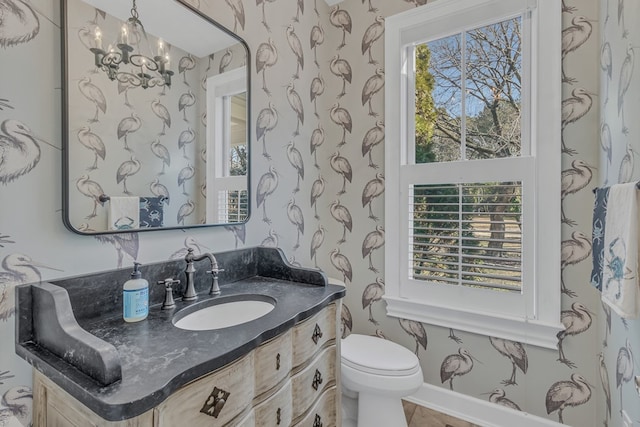 bathroom with an inviting chandelier, vanity, toilet, and wallpapered walls