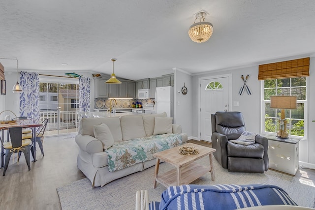 living area with vaulted ceiling, light wood-type flooring, a textured ceiling, and baseboards