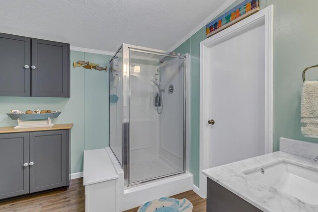full bath featuring a textured ceiling, baseboards, wood finished floors, a shower stall, and vanity