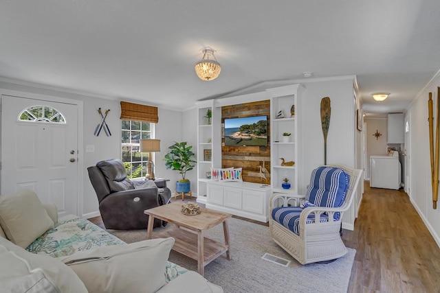 living room with visible vents, built in features, wood finished floors, washer / clothes dryer, and crown molding