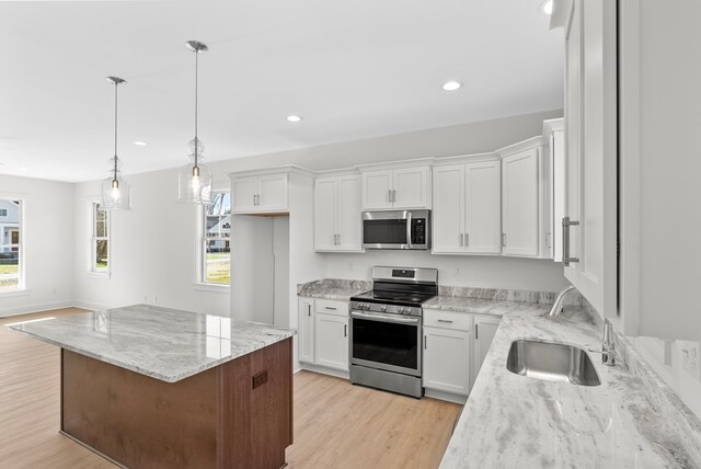 kitchen featuring stainless steel appliances, sink, a center island, white cabinetry, and hanging light fixtures