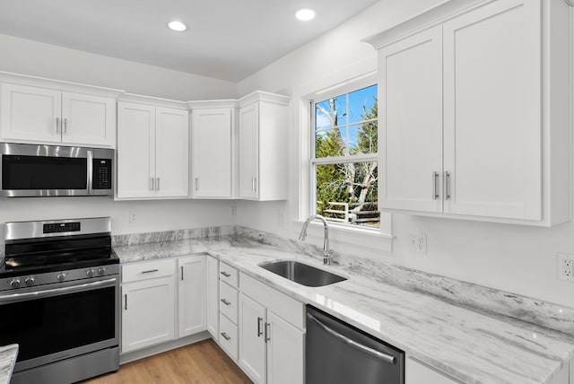 kitchen featuring light wood-style flooring, light stone counters, stainless steel appliances, white cabinetry, and a sink