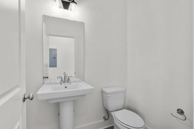 bathroom with electric panel, toilet, and baseboards