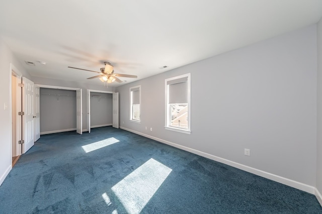 unfurnished bedroom featuring multiple closets, dark colored carpet, and ceiling fan