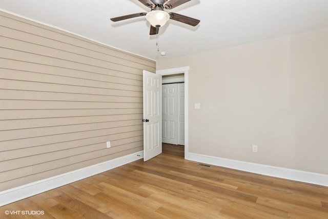 unfurnished bedroom with baseboards, wood walls, visible vents, and light wood finished floors