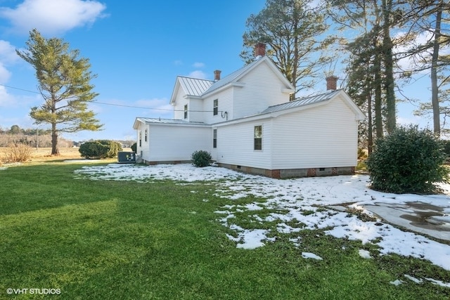 snow covered back of property featuring metal roof, a yard, a standing seam roof, and a chimney