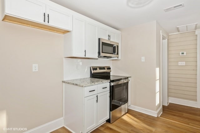 kitchen with light stone counters, stainless steel appliances, visible vents, white cabinetry, and light wood-type flooring