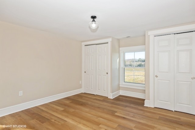 unfurnished bedroom featuring wood finished floors, two closets, and baseboards