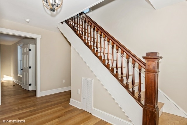 stairway featuring a notable chandelier, baseboards, visible vents, and wood finished floors