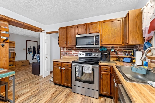 kitchen with sink, light hardwood / wood-style floors, a textured ceiling, and appliances with stainless steel finishes