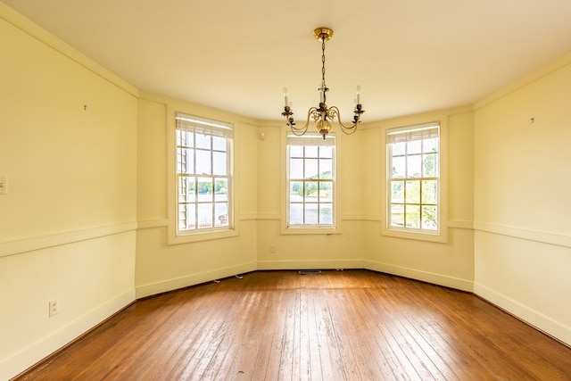 empty room featuring wood-type flooring, ornamental molding, and a chandelier