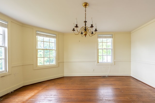 spare room featuring a healthy amount of sunlight, hardwood / wood-style flooring, crown molding, and a notable chandelier