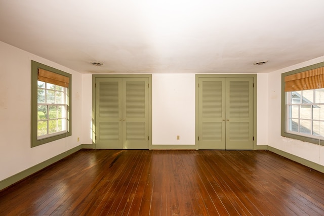 unfurnished bedroom featuring dark hardwood / wood-style flooring and two closets