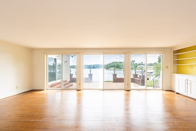 empty room with a water view, built in features, and light hardwood / wood-style flooring