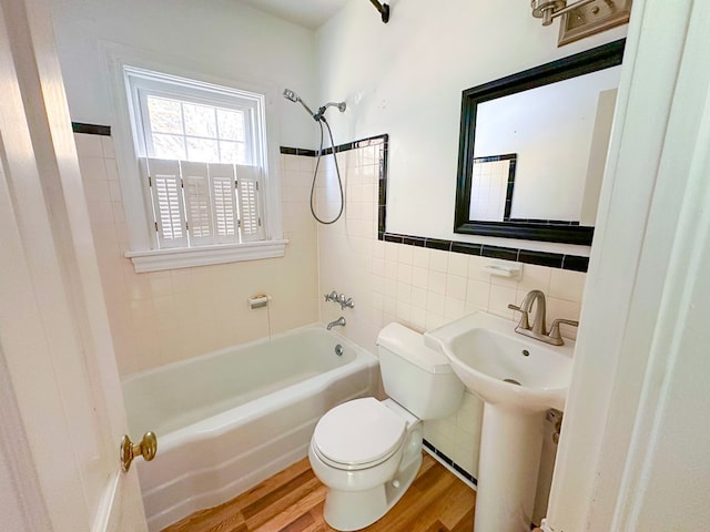 full bathroom with toilet, sink, wood-type flooring, tile walls, and tiled shower / bath combo