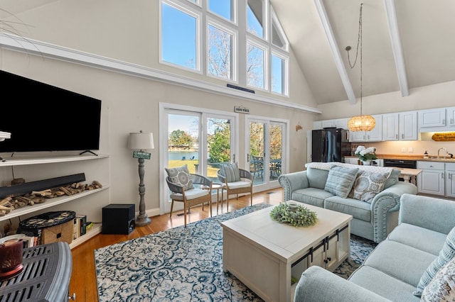 living room featuring high vaulted ceiling, sink, beamed ceiling, light hardwood / wood-style floors, and a chandelier